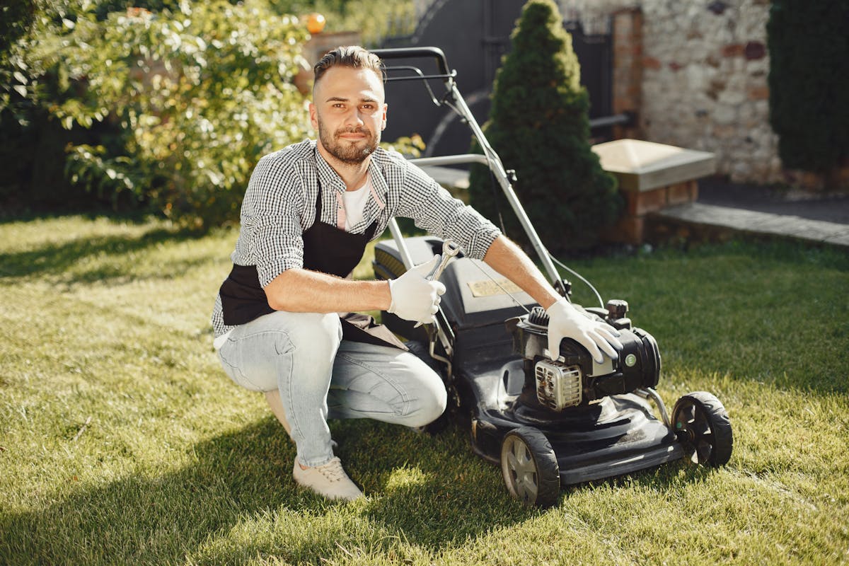 Man med förkläde och handskar som installerar och underhåller gräsklippare i trädgård — visar moment i installation utan slinga