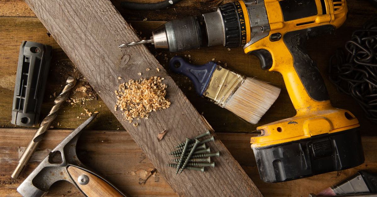 A close-up of various tools including a drill, hammer, and paintbrush on a wooden workbench.