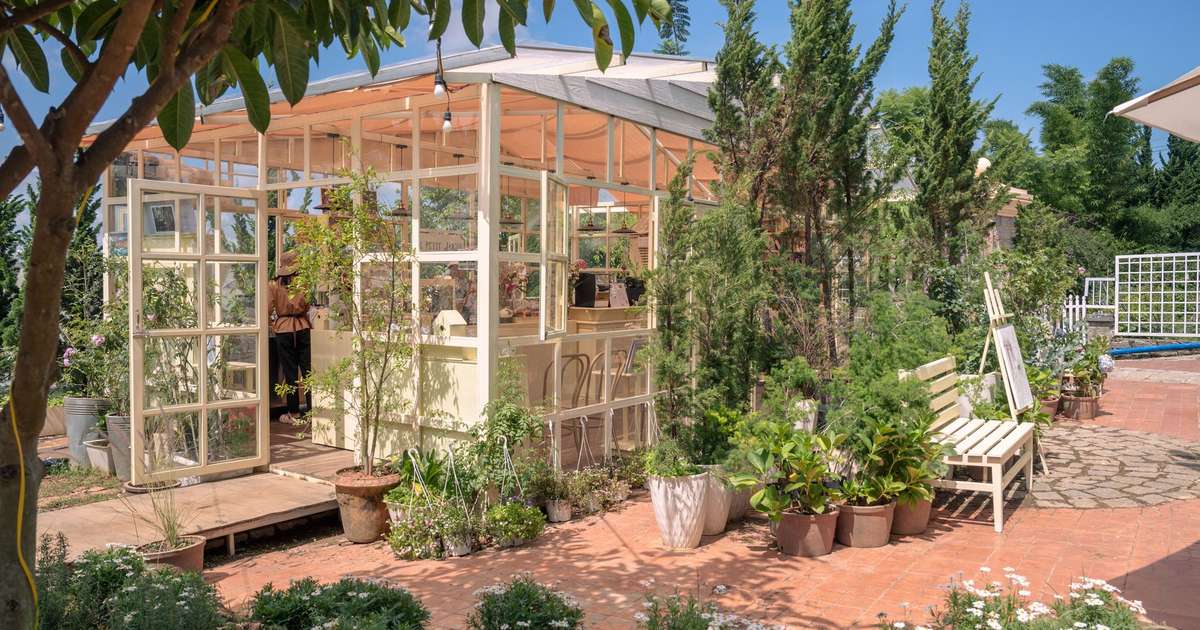 A sunlit greenhouse surrounded by lush greenery and blooming flowers in a peaceful garden.
