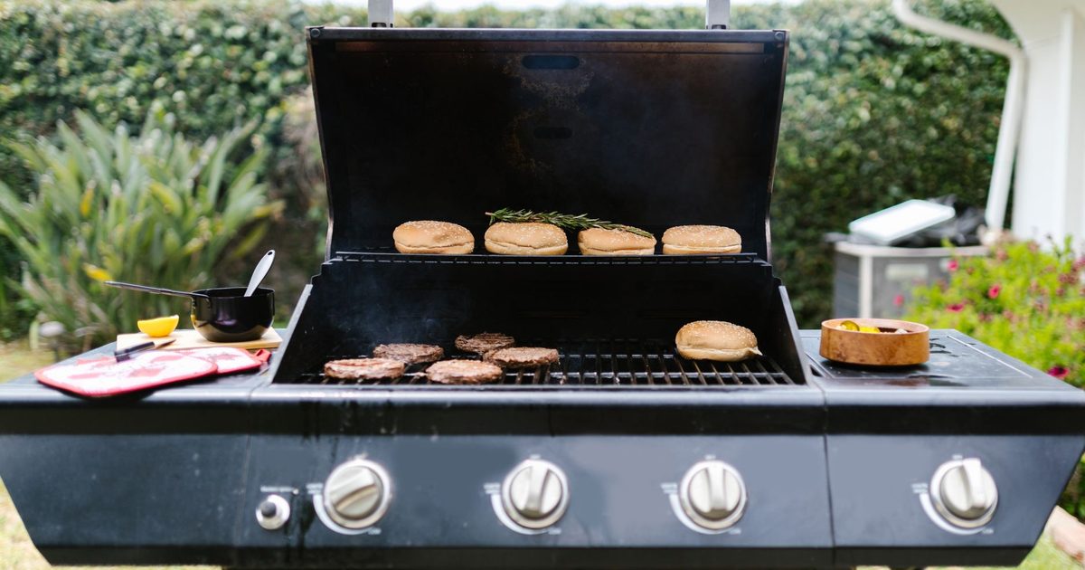 Modern svart gasolgrill med oppet lock pa en terrass, redo for grillning