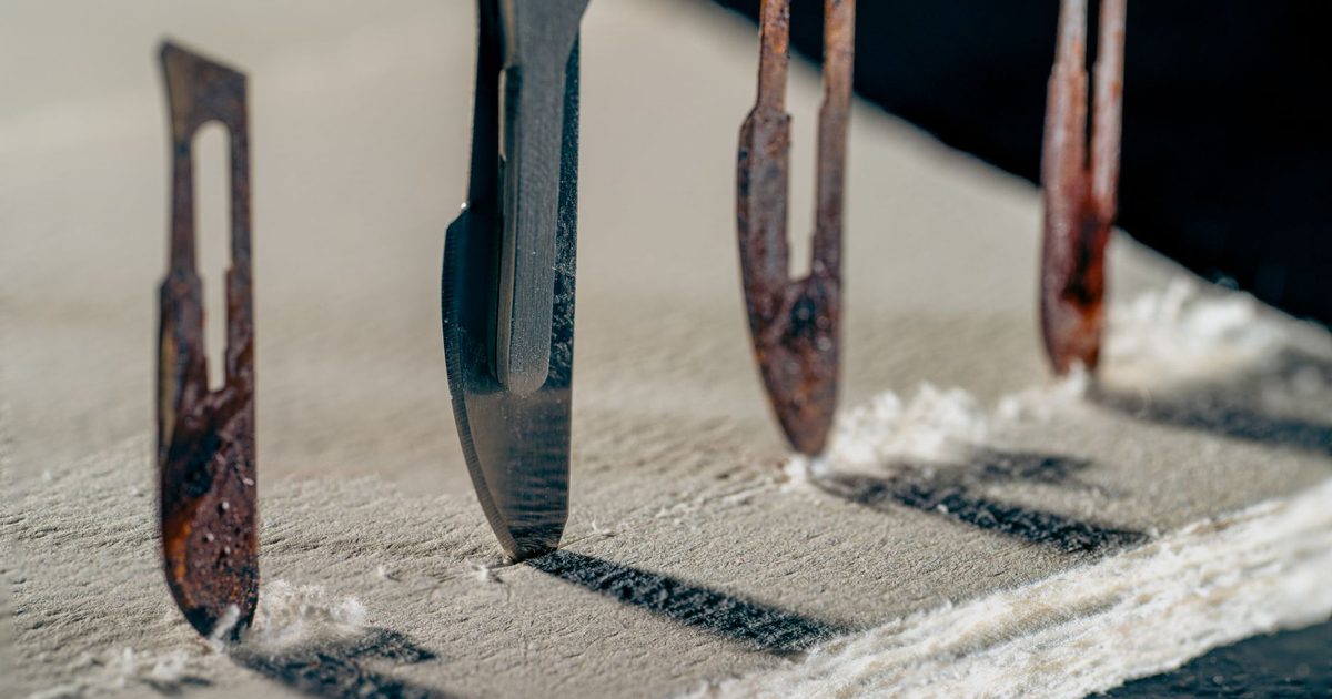 Detailed view of old and rusty scalpel blades lined up on a textured surface casting shadows.