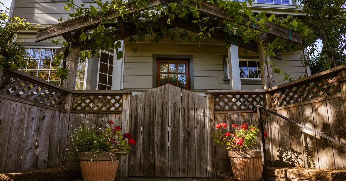 Trästaket med grind framför ett ljust trähus med blomkrukor vid ingången